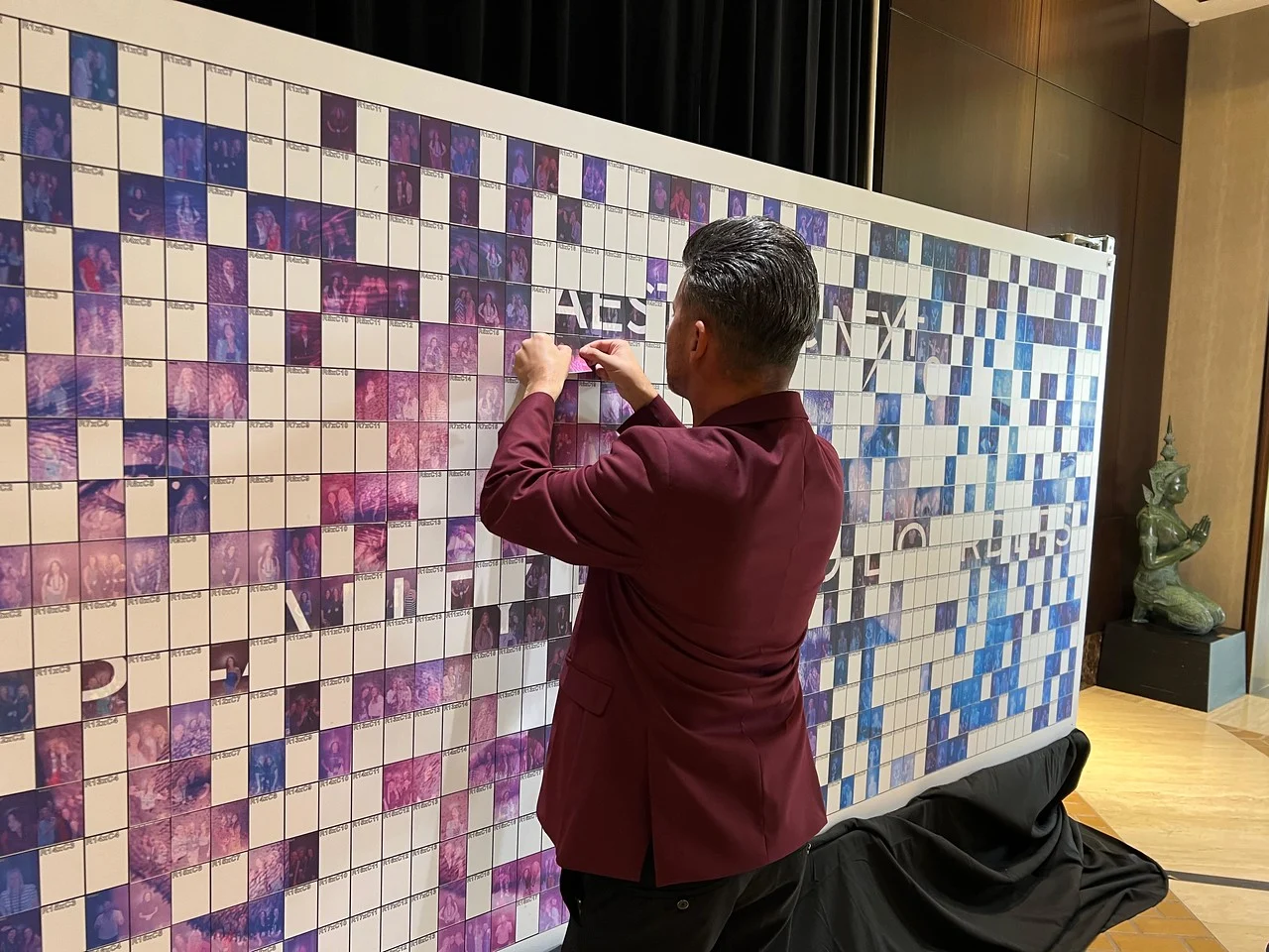 Person applying stickers to a mosaic wall featuring various images, showcasing guest participation in an interactive event activation by Firefly Creative Event Solutions.